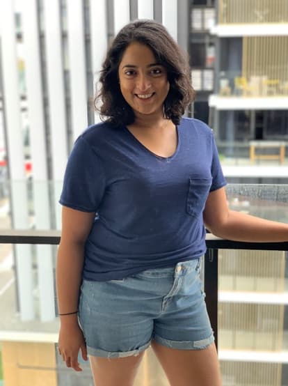 Priya Payda stands near a railing wearing a navy blue t-shirt and jean shorts.