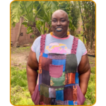 Image of Vanessa Rochelle in colorful overalls standing among ferns.